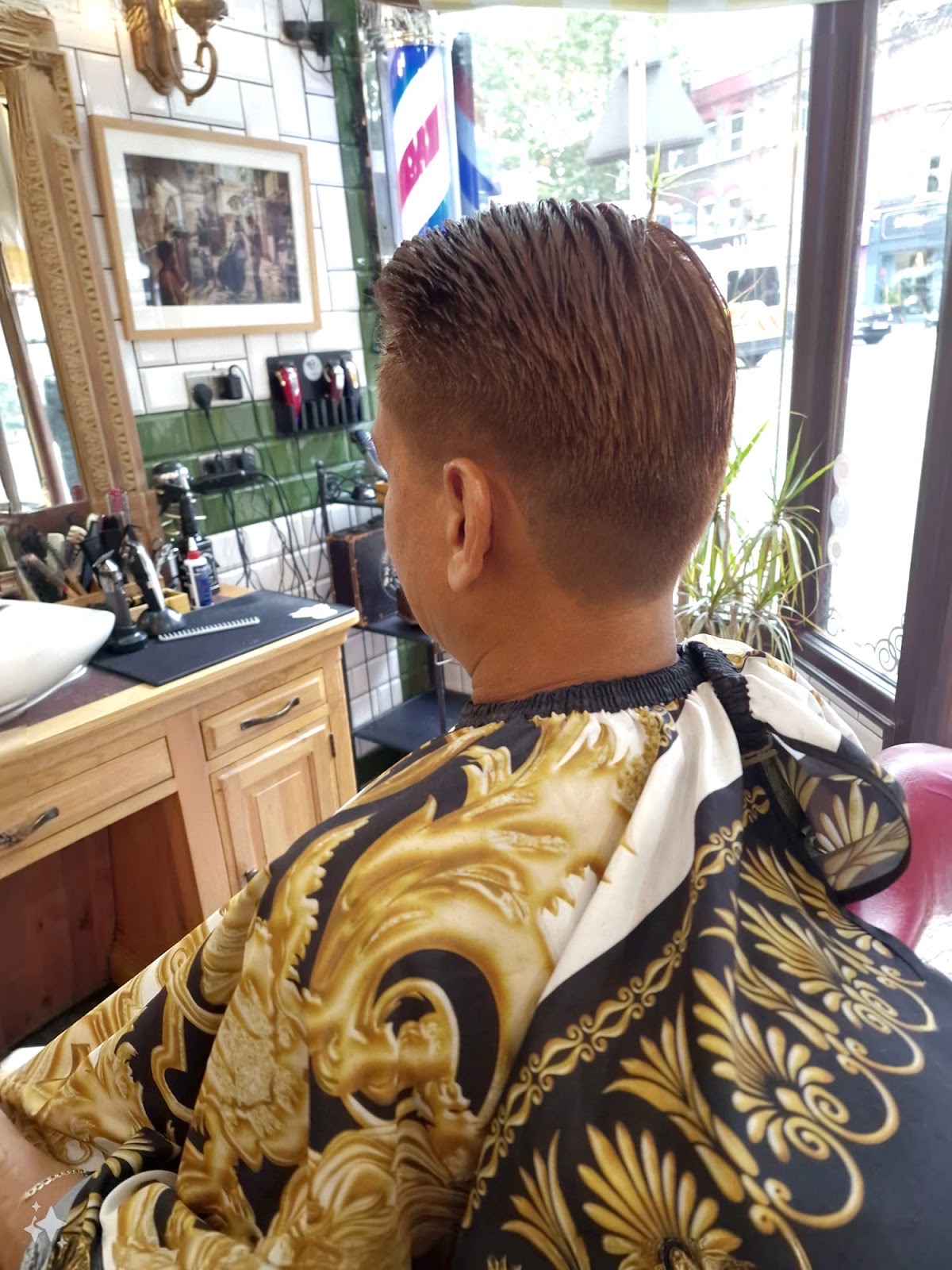Back view of a client in a gold gown with a slicked tapered cut, the shop window behind
